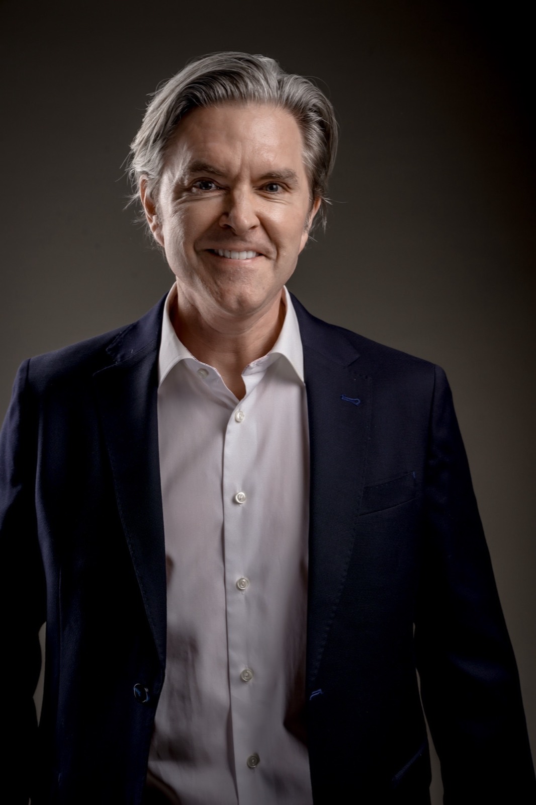 Matt Fraleigh, smiling, in a navy jacket against a dark background